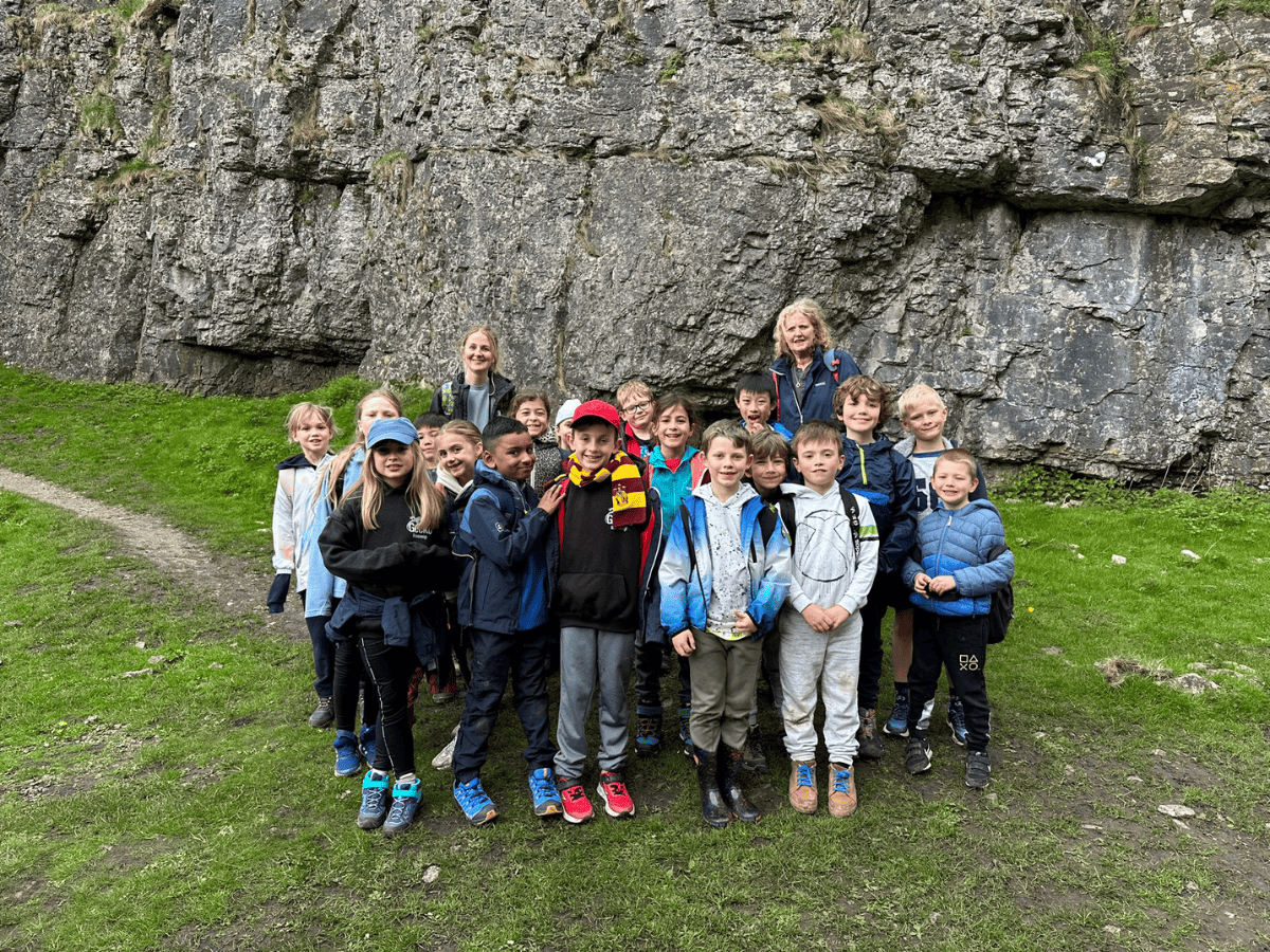 A group of Gorsey Bank Year 3 pupils smile in front of a scenic countryside background during a walk.